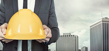 Businessman holding yellow helmet in hands on cityscape background